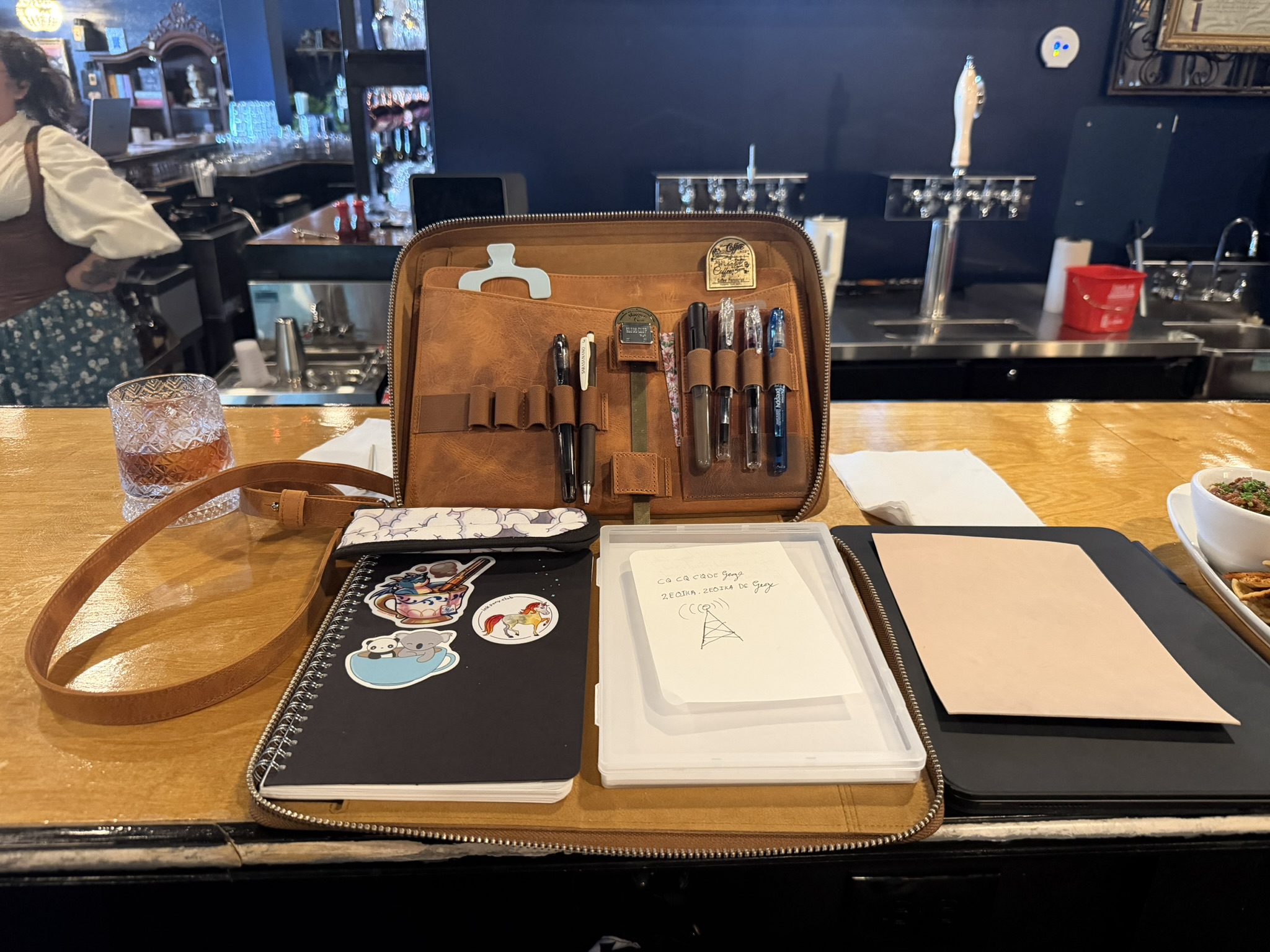 A leather pen case open on a table with fountain pens, notebooks, correspondence materials, and stationery tools.