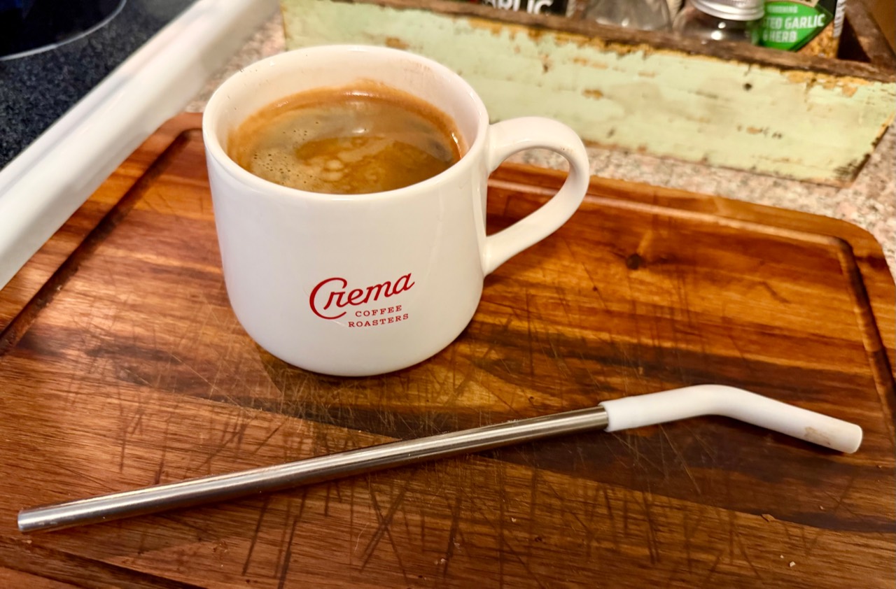An Americano in a white Crema Coffee Roasters mug on a wooden cutting board.