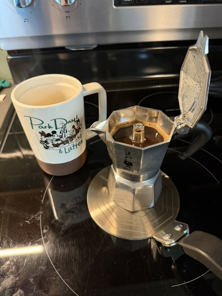 A Bialetti moka pot beside a Disney-themed Park Days and Lattes mug in a Fort Wilderness cabin kitchen.