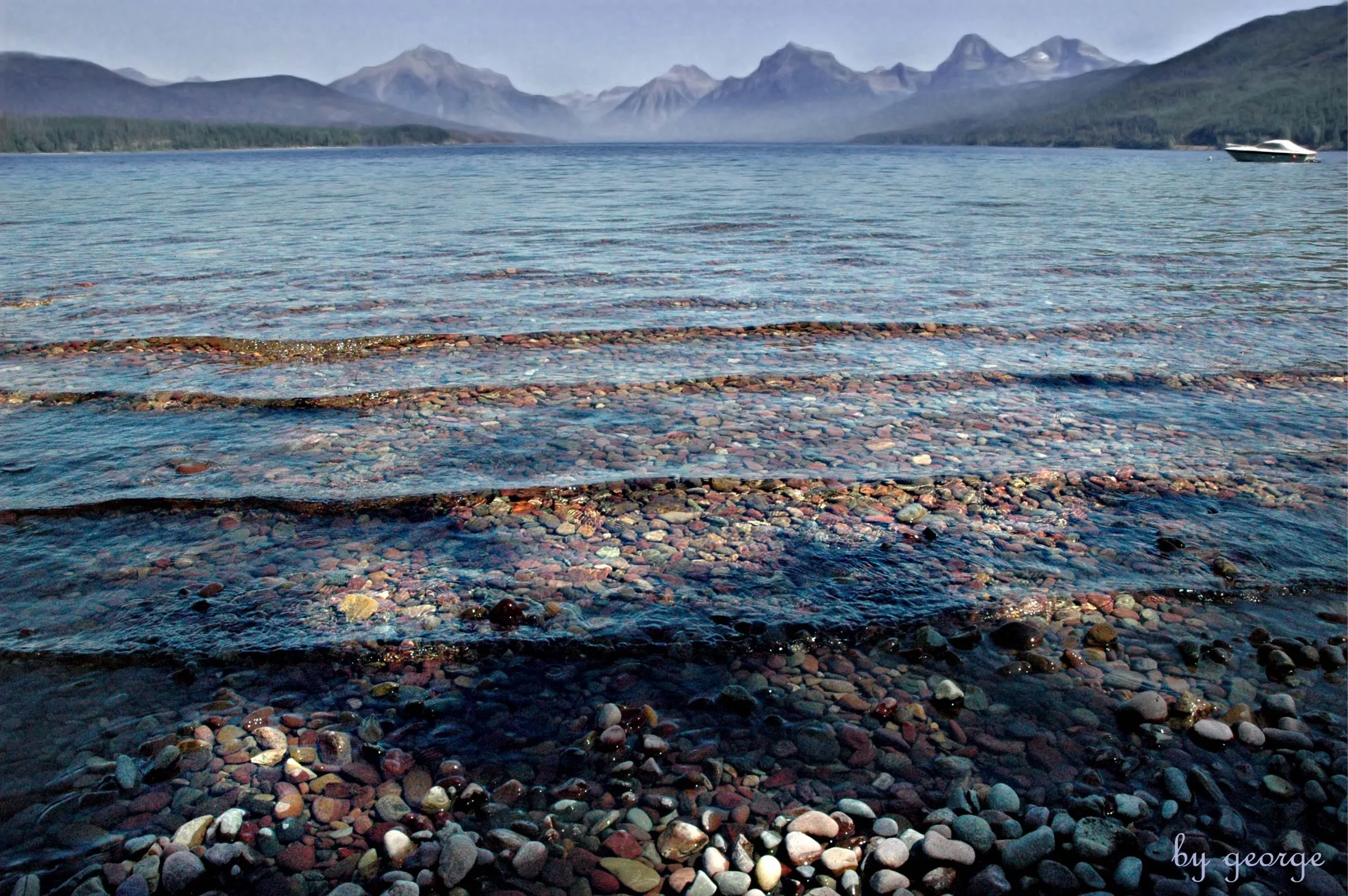 Clear shallow water over smooth stones with mountains in the distance.